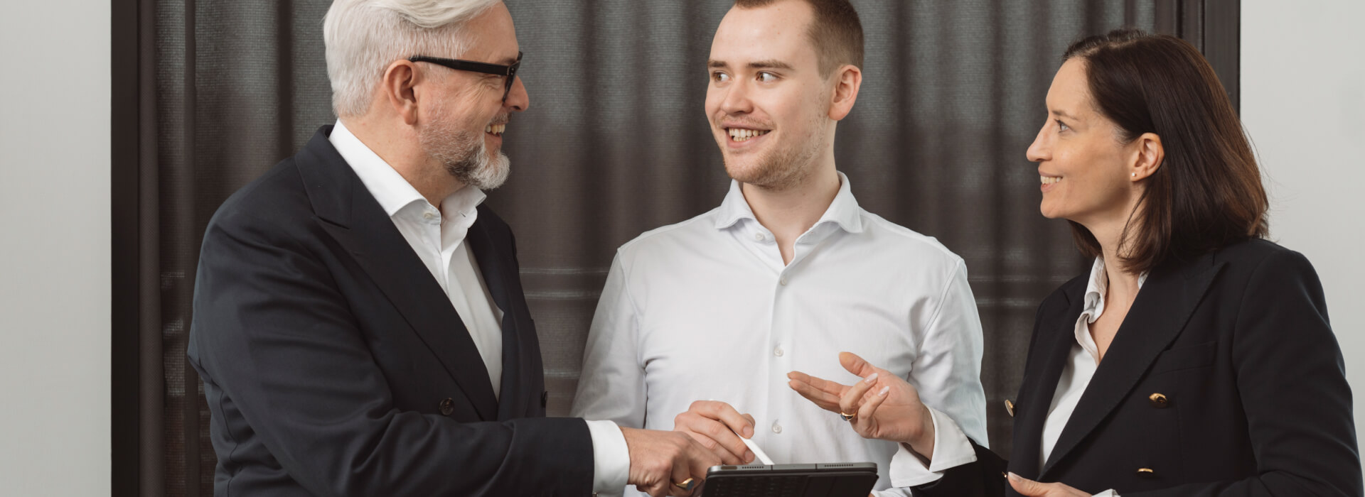 Drei Personen stehen im Büro zusammen und besprechen Consulting Services anhand eines Tablets.