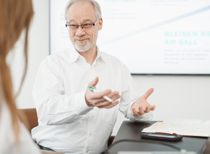 Mitarbeiter erkl&auml;rt in einem Meeting Aspekte der digitalen Transformation, w&auml;hrend Unterlagen und ein Laptop auf dem Tisch liegen.