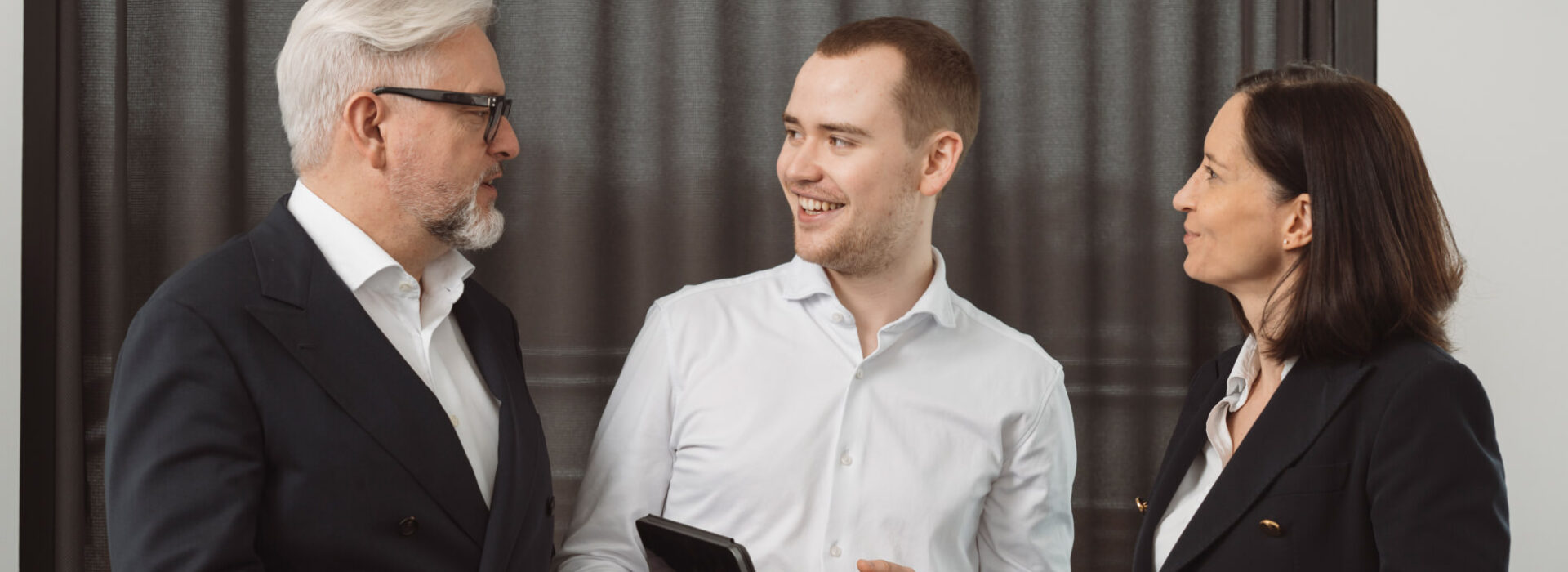 Drei Personen in einer Business-Besprechung mit Tablet, konzentriert auf Strategie, Abstimmung und digitale Unternehmensprozesse.
