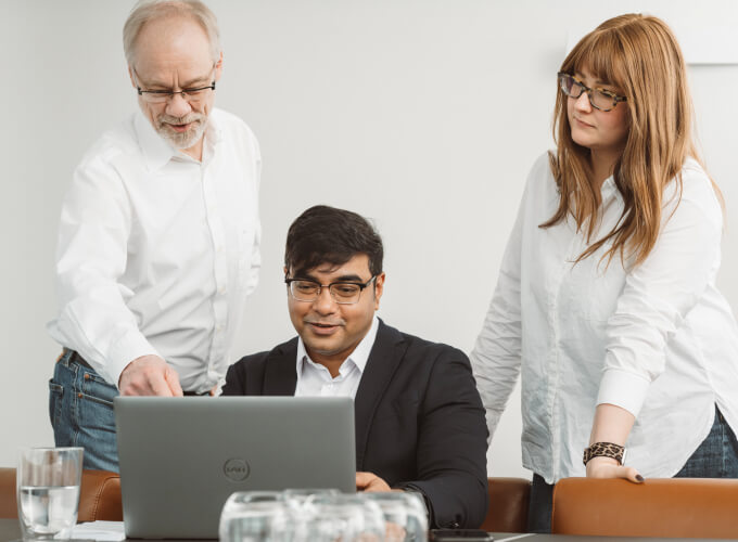 Drei Personen in einer Business-Besprechung arbeiten gemeinsam an einem Laptop und stimmen digitale Unternehmensprozesse ab.