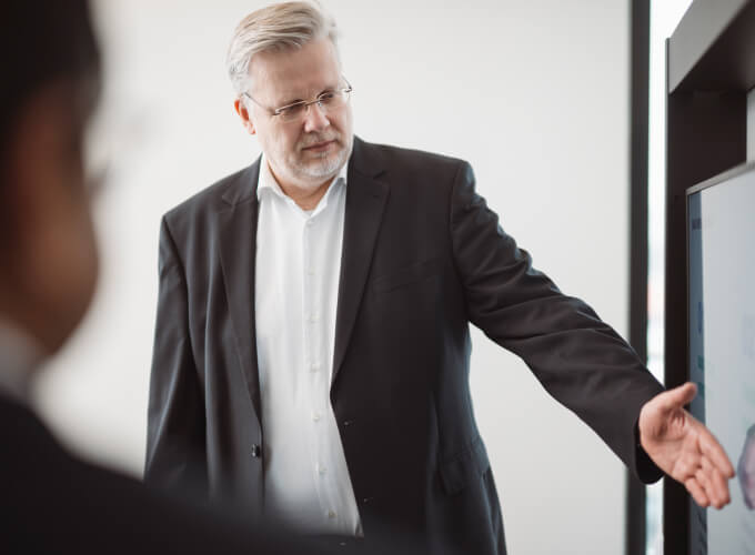 Gesch&auml;ftsmann erl&auml;utert an einem Bildschirm strukturierte Unternehmens- oder Finanzprozesse in einem Meeting.