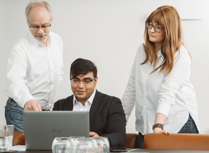 Drei Personen arbeiten gemeinsam an einem Laptop an ERP-Themen.