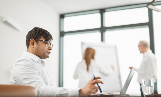 Drei Personen in einem Besprechungsraum bei einem Workshop zu Consulting Services, eine Person arbeitet am Laptop, zwei weitere stehen am Whiteboard.