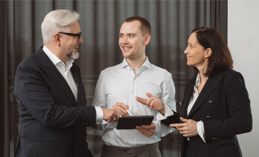 Drei Personen stehen im Büro zusammen und besprechen Consulting Services anhand eines Tablets.