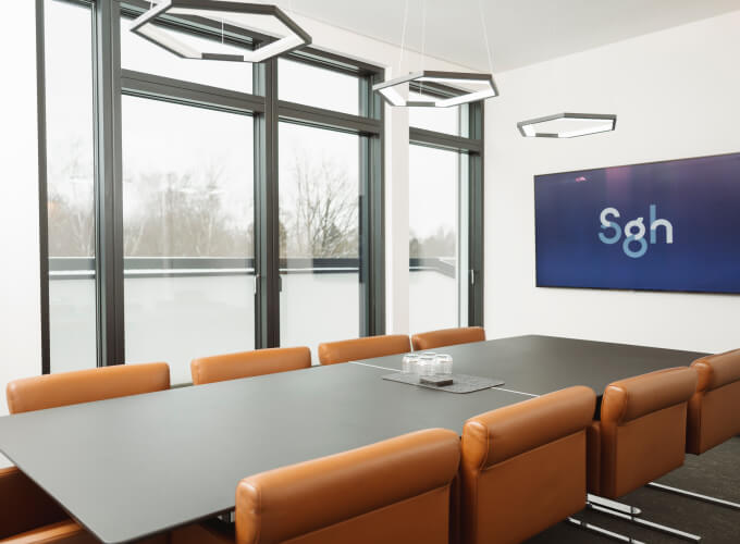 Moderner Besprechungsraum bei SGH mit Konferenztisch, Stühlen und Bildschirm an der Wand
