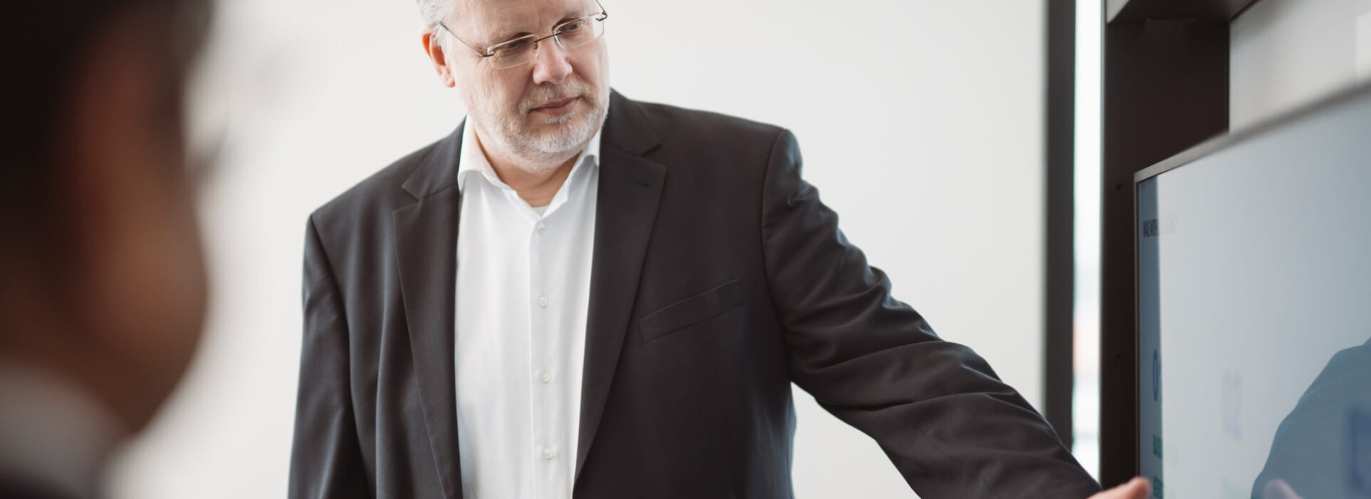 Geschäftsmann erläutert an einem Bildschirm strukturierte Unternehmens- oder Finanzprozesse in einem Meeting.