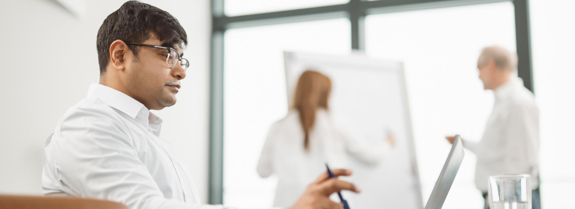 Drei Personen in einem Besprechungsraum bei einem Workshop zu Consulting Services, eine Person arbeitet am Laptop, zwei weitere stehen am Whiteboard.