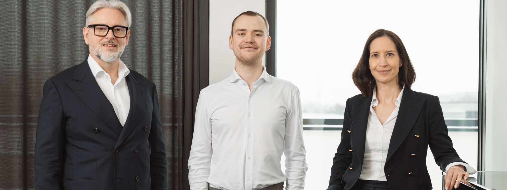 Drei Personen in Business-Kleidung stehen gemeinsam in einem modernen Büroumfeld.